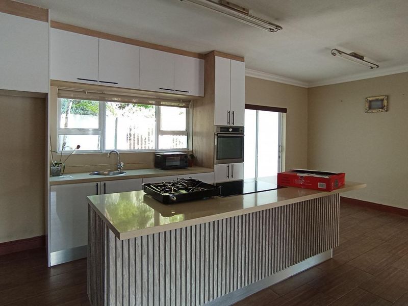 Spacious open-plan kitchen featuring modern cabinetry, stone countertops, a central island with a gas hob, and built-in oven, set against tiled flooring.