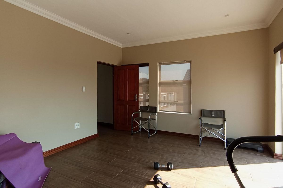 A spacious bedroom featuring tiled flooring, neutral wall tones, and natural light through a window with roller blinds.