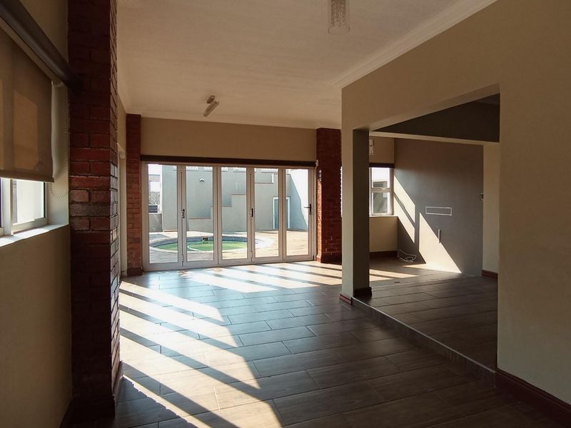 Spacious open-plan living area featuring tiled floors, exposed brick columns, and large folding glass doors providing direct access to the outdoor pool area.
