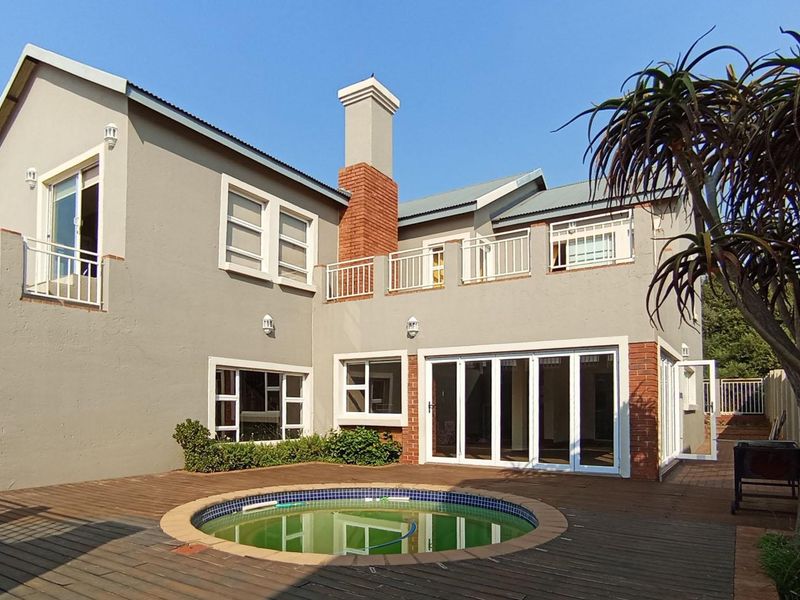 Rear exterior view featuring a circular swimming pool, timber decking, brick chimney, and balcony access from the upper level.
