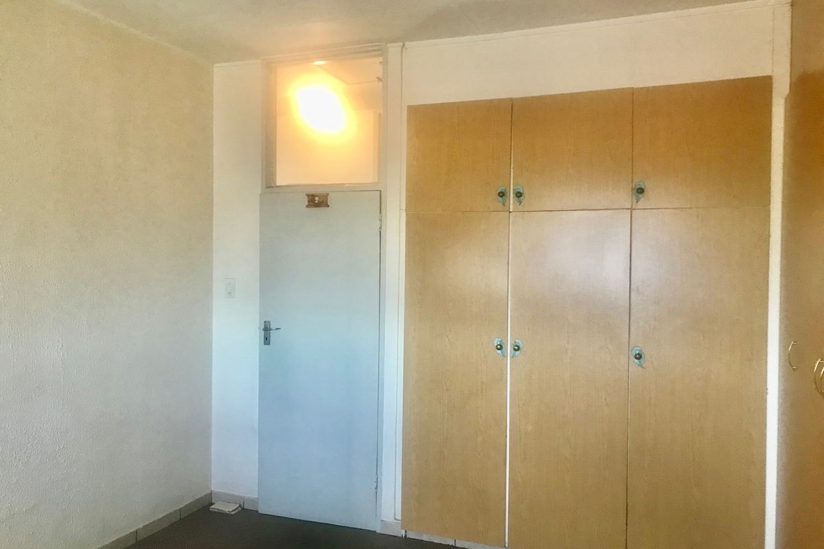 A vacant bedroom featuring built-in wooden cupboards, a transom window above the door, and neutral wall finishes, ready for modernization.
