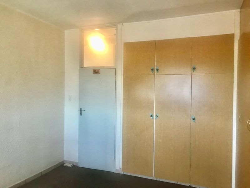 A vacant bedroom featuring built-in wooden cupboards, a transom window above the door, and neutral wall finishes, ready for modernization.