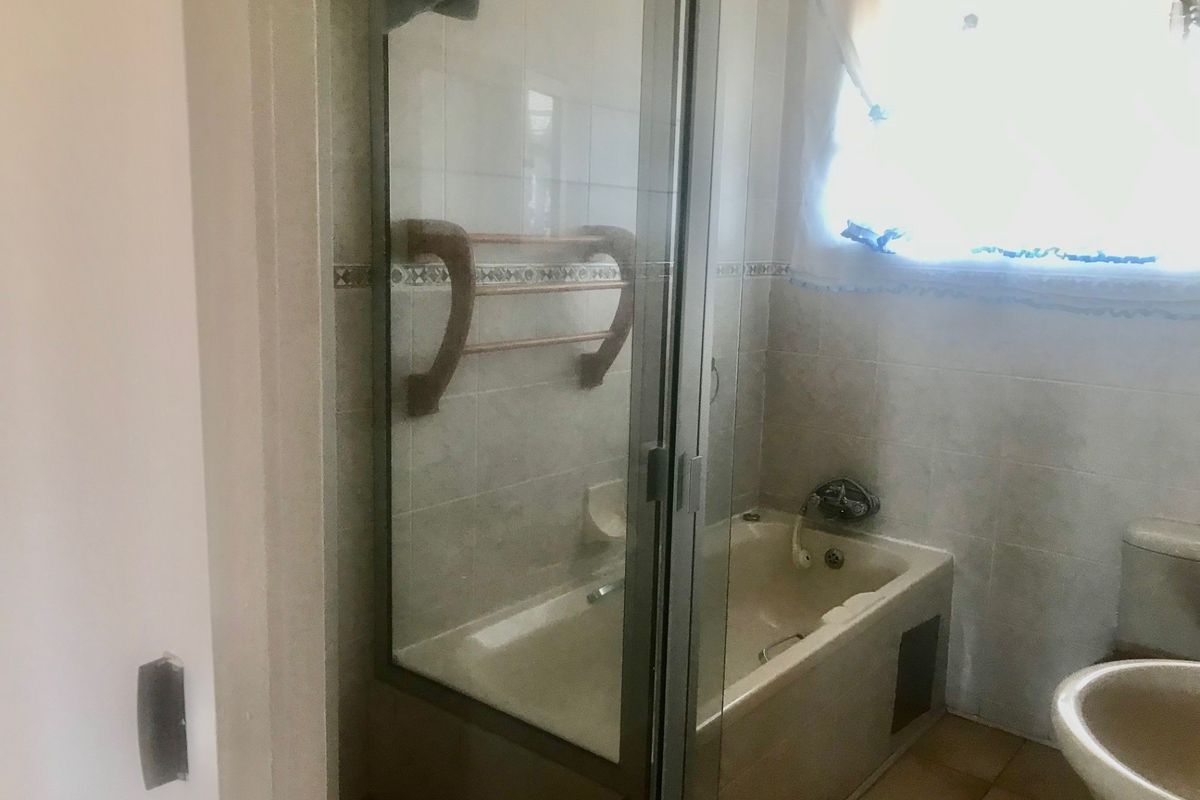 A dated bathroom featuring a combined shower and bathtub unit, ceramic tiling, and standard sanitary ware, requiring modernization to improve aesthetic appeal.