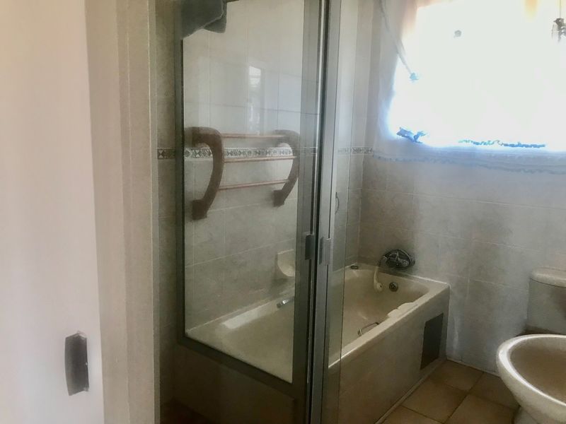 A dated bathroom featuring a combined shower and bathtub unit, ceramic tiling, and standard sanitary ware, requiring modernization to improve aesthetic appeal.