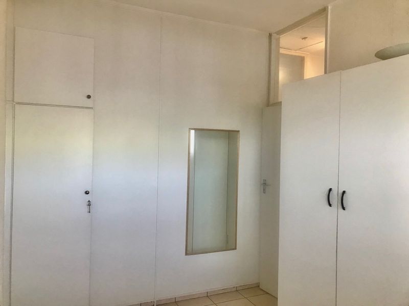A bedroom interior featuring white built-in cupboards, tiled flooring, and a transom window above the doorway.