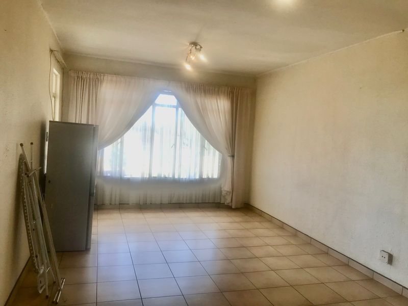 An empty living room featuring tiled flooring and a large window, providing a blank canvas for potential interior design and renovation.