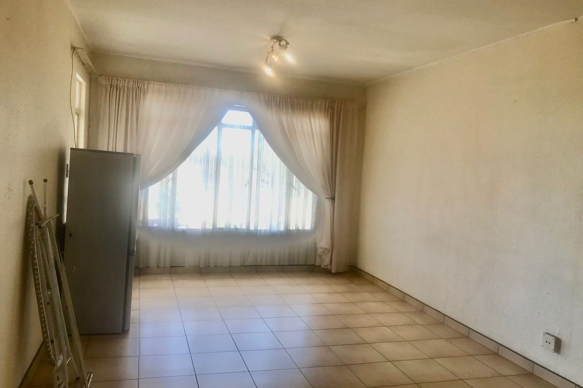 An empty living room featuring tiled flooring and a large window, providing a blank canvas for potential interior design and renovation.