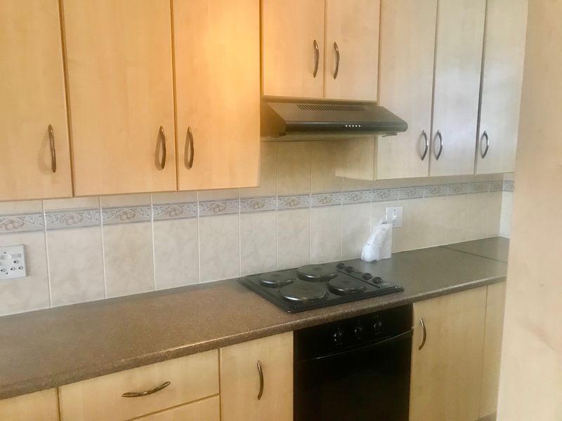 A functional kitchen featuring light wood-finish cabinetry, dark countertops, a built-in oven, electric hob, and a tiled backsplash.