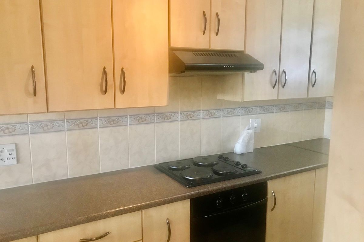 A functional kitchen featuring light wood-finish cabinetry, dark countertops, a built-in oven, electric hob, and a tiled backsplash.