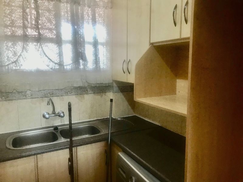 A compact kitchen featuring built-in cabinetry, a double bowl stainless steel sink, and laminate countertops, offering a functional space in need of modernization.
