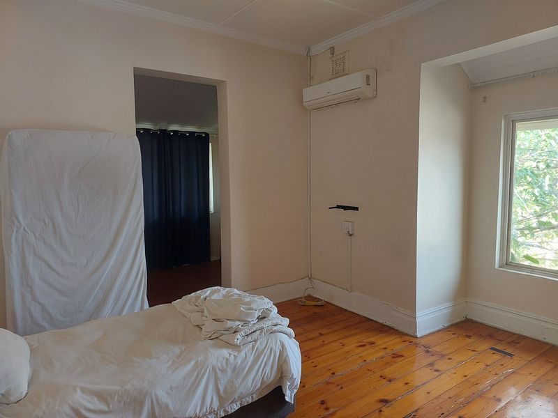 A bedroom featuring original timber flooring, a wall-mounted air conditioning unit, and neutral wall finishes, offering a blank canvas for renovation.