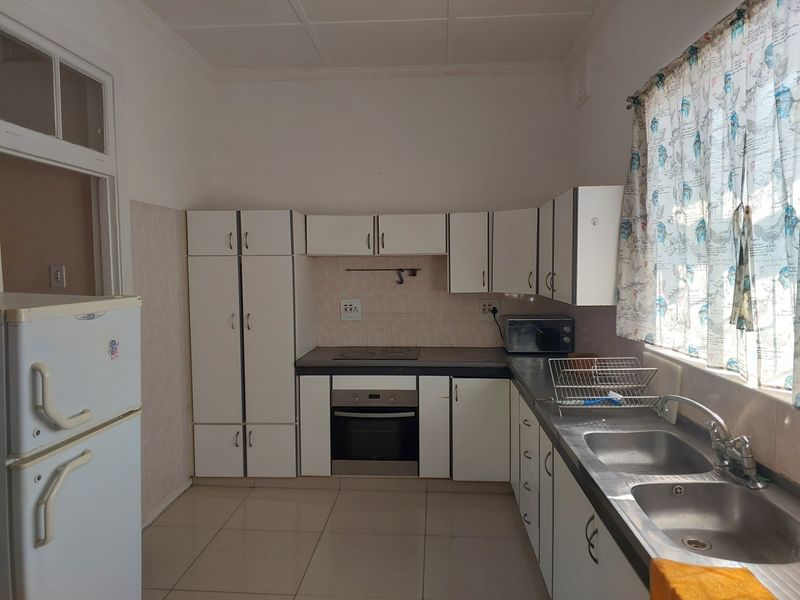 A functional kitchen featuring white built-in cabinetry, a stainless steel double sink, an electric hob, and an integrated oven with tiled flooring.
