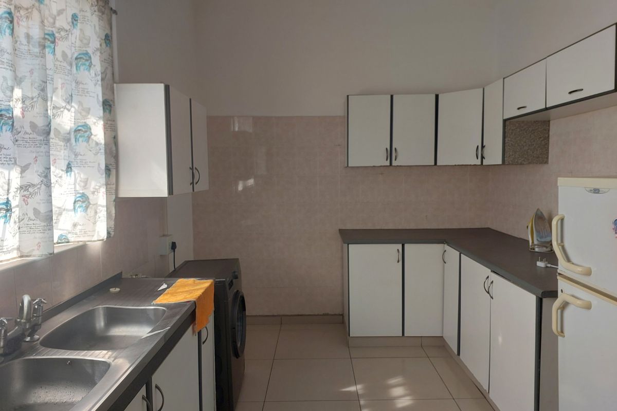 A functional kitchen featuring white cabinetry, laminate countertops, a double basin stainless steel sink, and tiled splashbacks with neutral floor tiles.