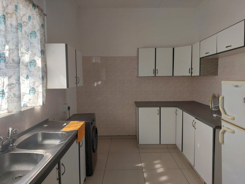 A functional kitchen featuring white cabinetry, laminate countertops, a double basin stainless steel sink, and tiled splashbacks with neutral floor tiles.