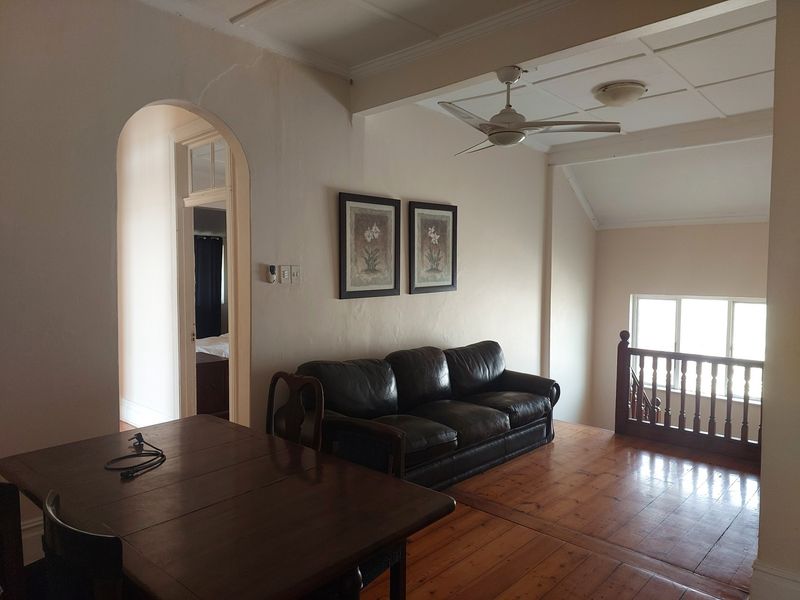 Spacious living area featuring original hardwood flooring, a ceiling fan, and an arched doorway leading to adjacent rooms, with a classic wooden balustrade.