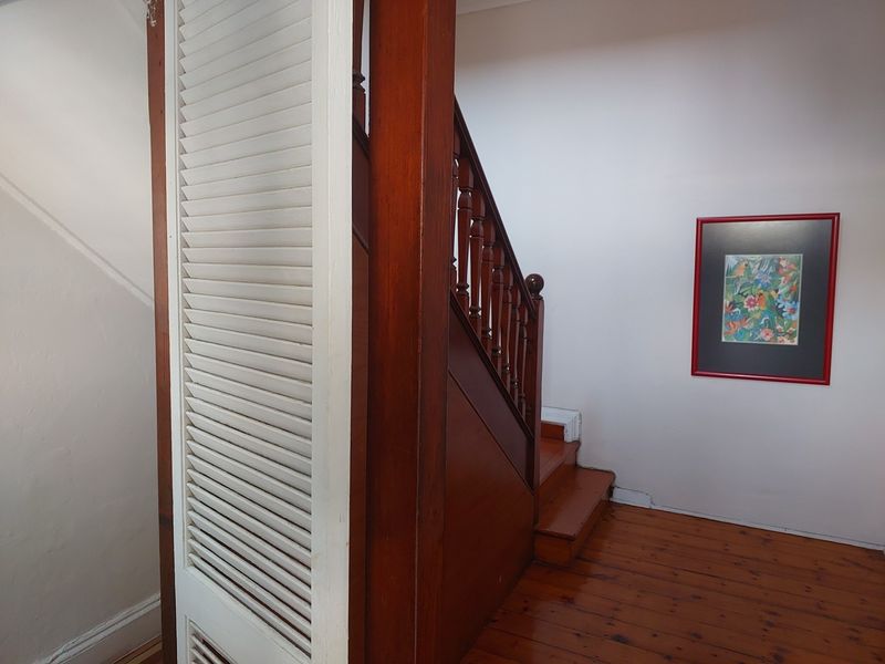 A hallway featuring polished timber flooring and a traditional timber staircase with a matching balustrade, complemented by a louvered door.