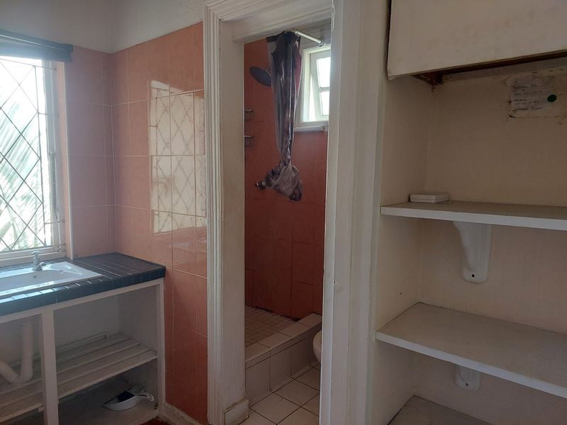A dated bathroom featuring a tiled vanity, built-in storage shelving, and a separate shower enclosure with pink wall tiling.
