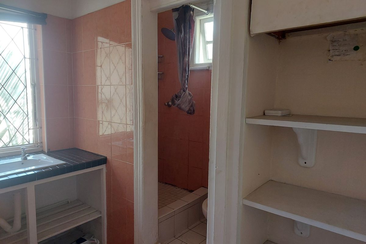 A dated bathroom featuring a tiled vanity, built-in storage shelving, and a separate shower enclosure with pink wall tiling.