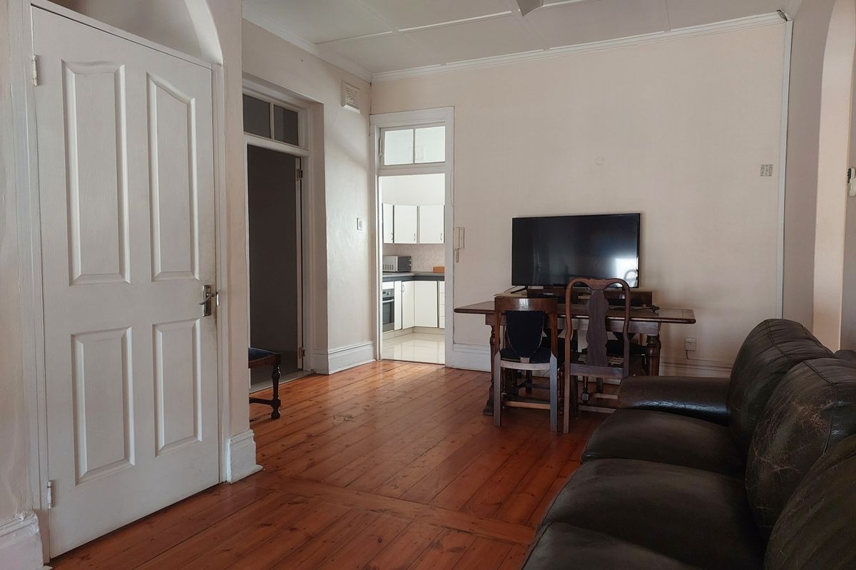 A living room featuring original timber flooring, high ceilings with panelled detailing, and an arched doorway leading to an adjacent kitchen area.