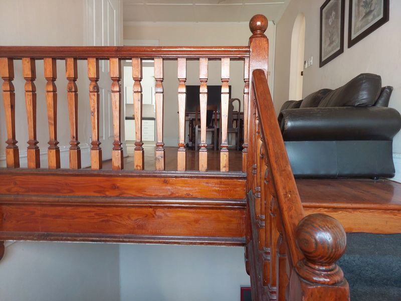 A view from the top of a timber staircase featuring a traditional wooden balustrade and handrail, leading into an open plan living area.