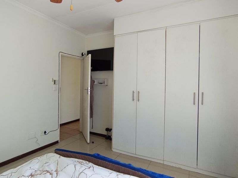 A bedroom featuring built-in cupboards, tiled flooring, and a ceiling fan, with visible surface-mounted electrical wiring near the doorway.