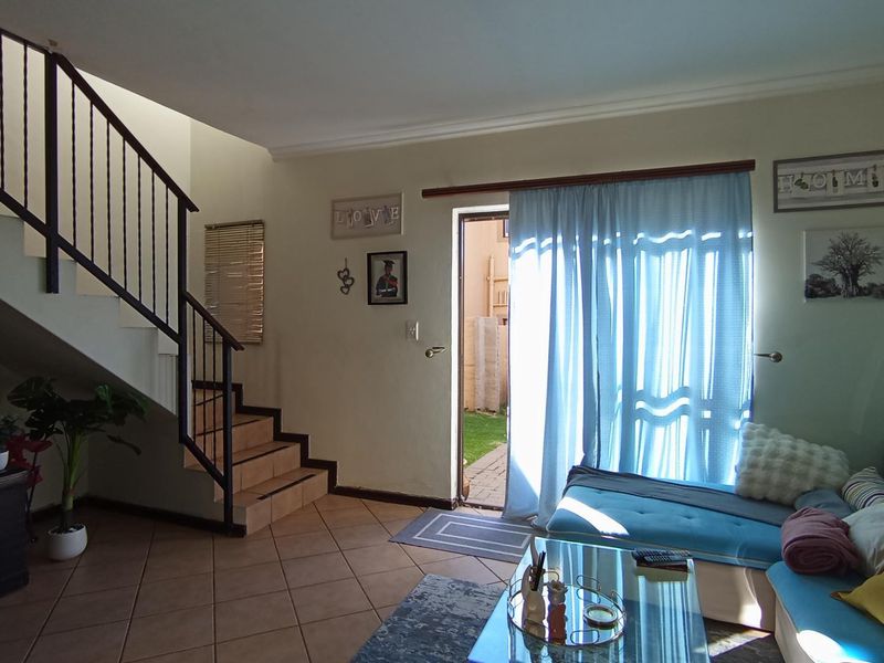 Living room featuring tiled flooring, a staircase with a metal balustrade, and direct access to the rear garden through a sliding door.