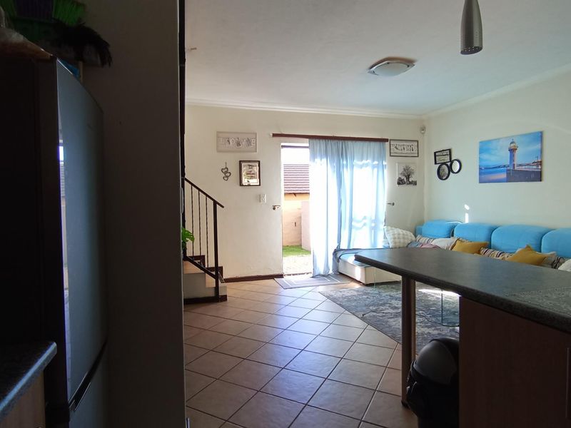Open-plan living area featuring tiled flooring, a breakfast bar, and a staircase, with direct access to the outdoor space through a sliding door.