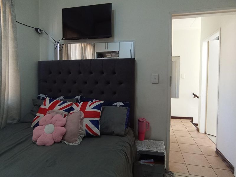 A bedroom featuring a wall-mounted television and mirrored accent panel, with an adjacent tiled hallway visible through the doorway.