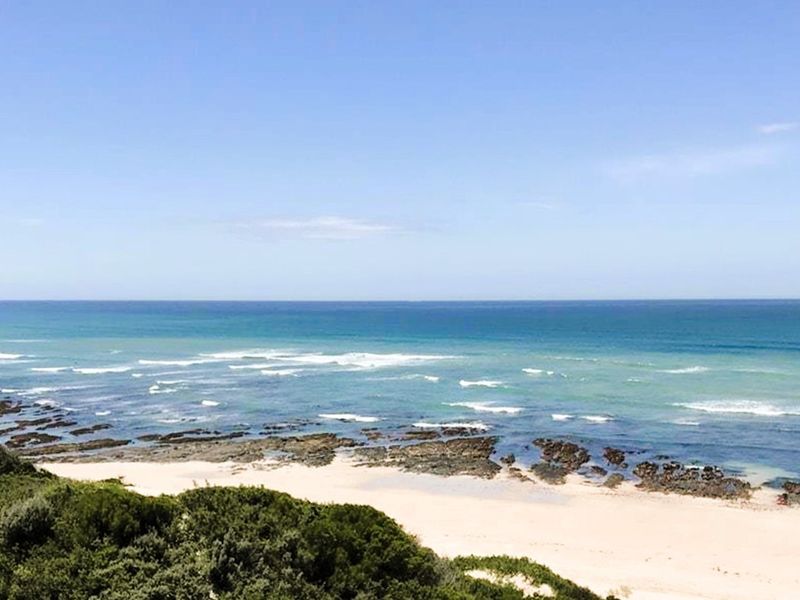 A scenic elevated view of the ocean, sandy beach, and rocky coastline, showcasing the natural beauty of the property's surroundings.
