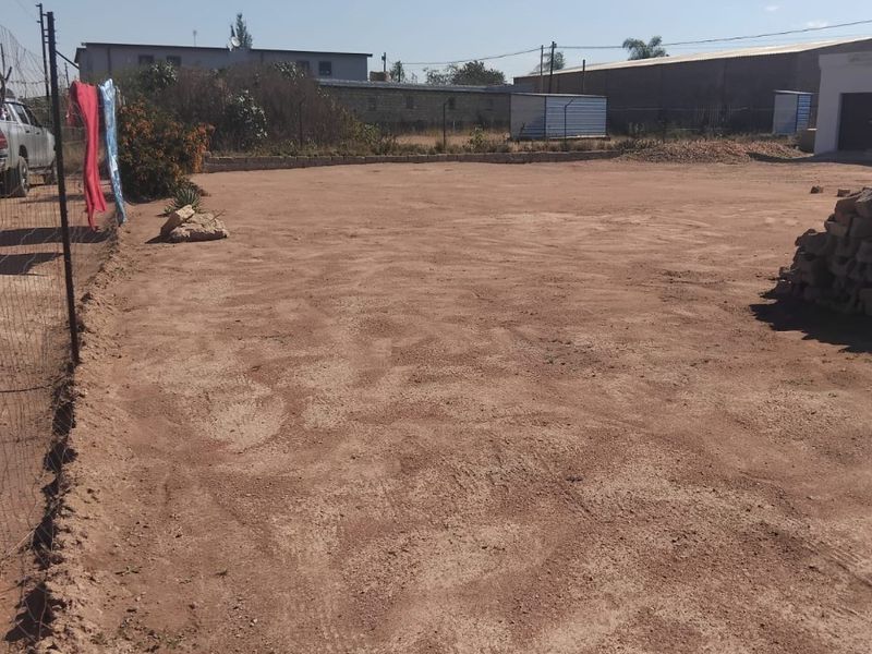 A vacant residential plot featuring cleared earth, wire mesh perimeter fencing, and a low retaining wall, offering a blank canvas for development.