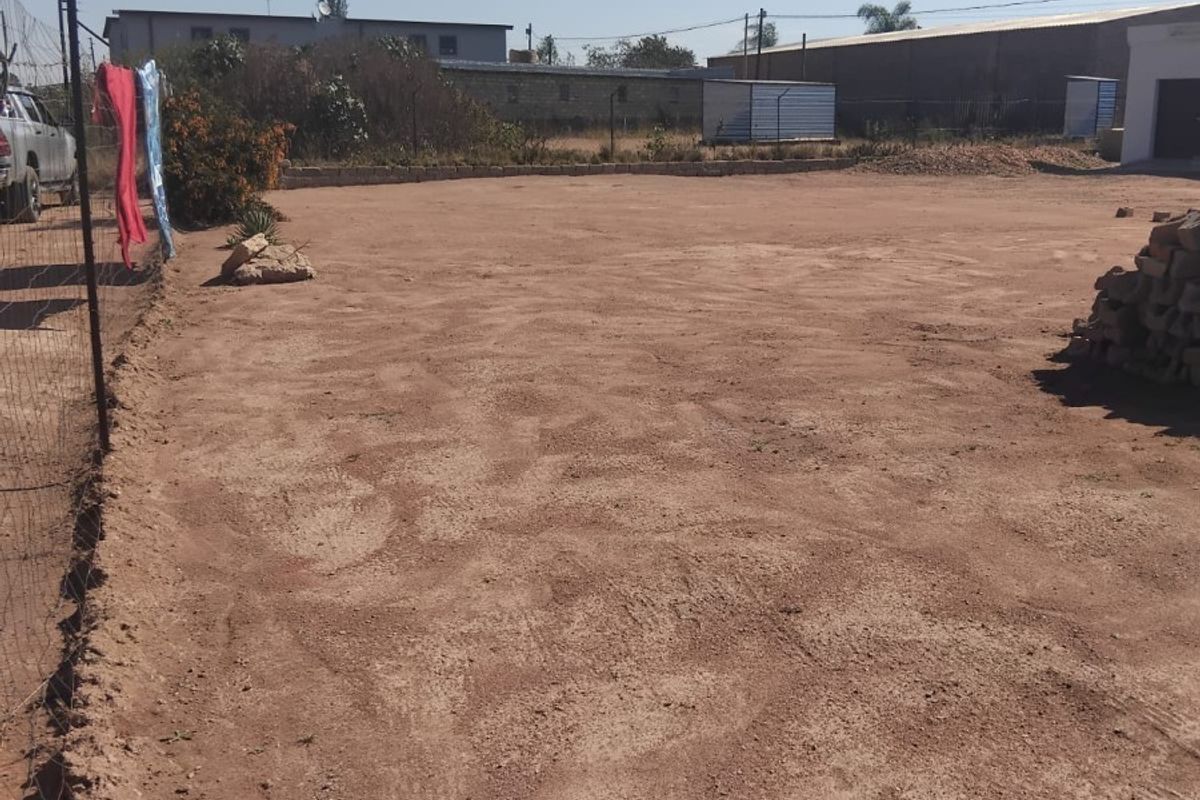 A vacant residential plot featuring cleared earth, wire mesh perimeter fencing, and a low retaining wall, offering a blank canvas for development.