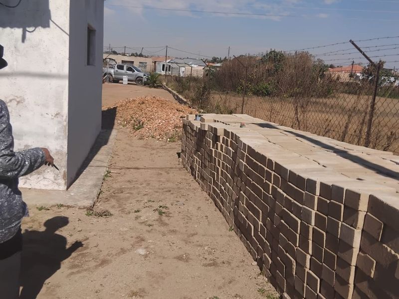 View of the rear exterior area of the property featuring a chain-link fence and unpaved ground.