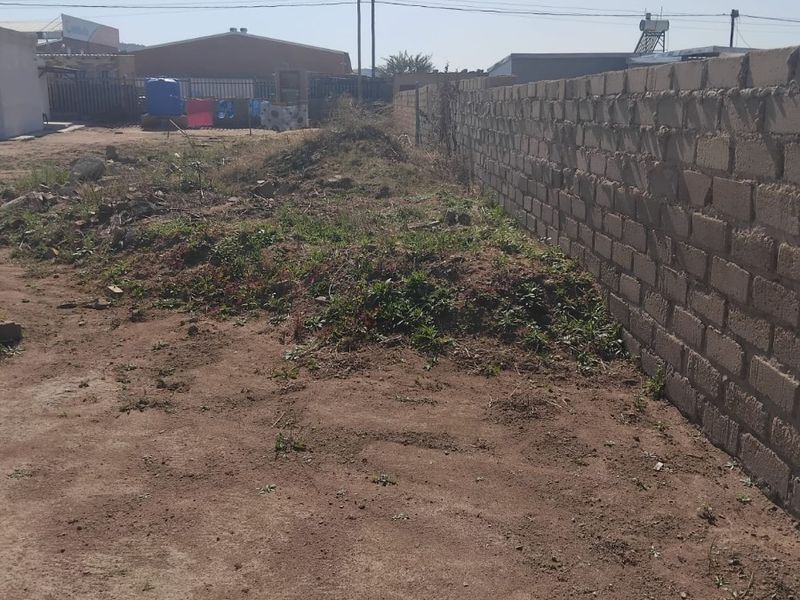 A view of a vacant residential plot featuring an existing perimeter brick wall and uneven, undeveloped ground.