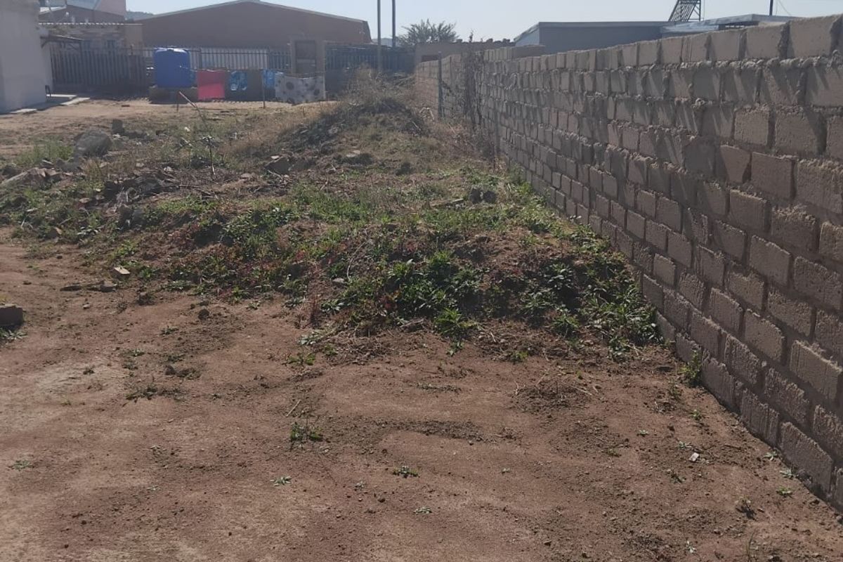 A view of a vacant residential plot featuring an existing perimeter brick wall and uneven, undeveloped ground.