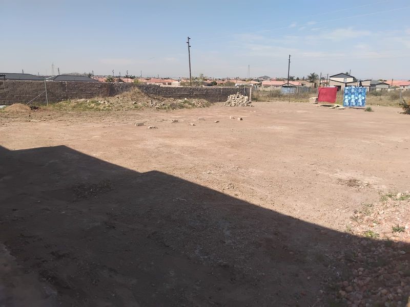 A view of a vacant residential plot featuring a perimeter wall and open ground, suitable for future development.