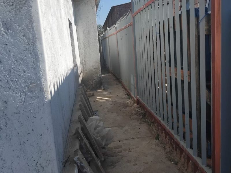 A narrow side passage featuring a concrete walkway, perimeter wall with security spikes, and unfinished exterior wall surfaces.