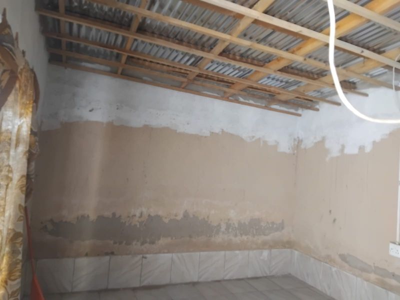 An unfinished interior room featuring exposed timber roof trusses, corrugated metal ceiling, and tiled flooring, requiring significant renovation and wall finishing.
