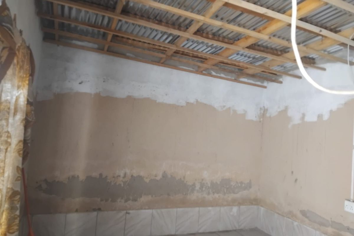An unfinished interior room featuring exposed timber roof trusses, corrugated metal ceiling, and tiled flooring, requiring significant renovation and wall finishing.