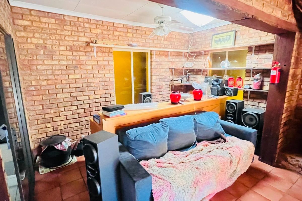Living room featuring exposed brick walls, timber ceiling beams, and terracotta floor tiles, offering a rustic aesthetic with built-in shelving.