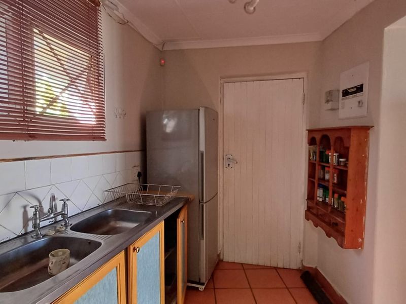 A functional kitchen area featuring a double stainless steel sink, tiled splashback, and tiled flooring, offering potential for modernization and cosmetic updates.