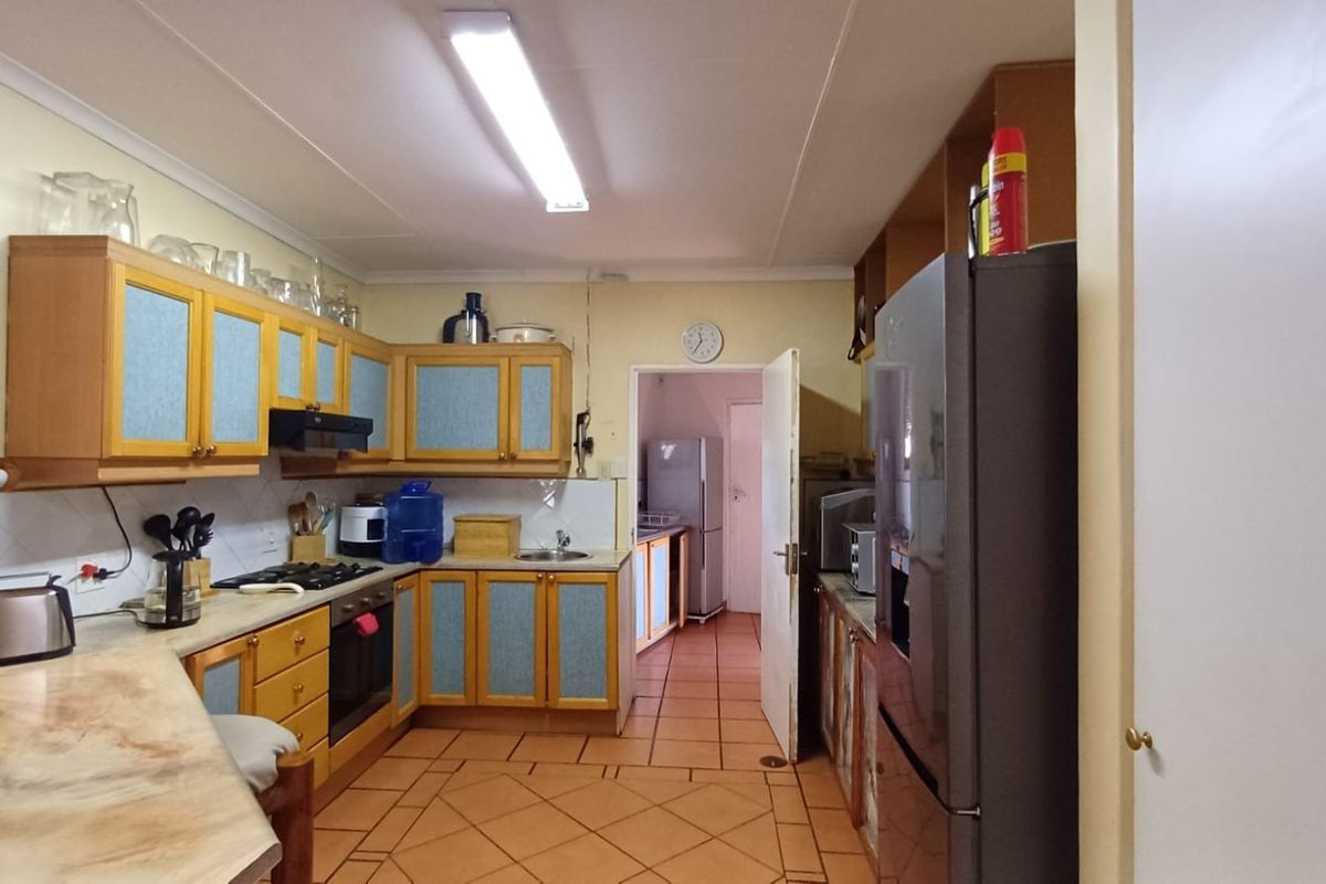 A functional kitchen featuring dated wooden cabinetry, laminate countertops, built-in oven, gas hob, and tiled flooring, with an adjacent scullery area visible.