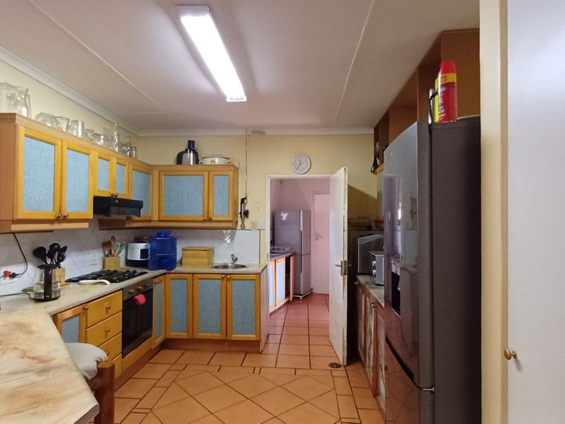 A functional kitchen featuring dated wooden cabinetry, laminate countertops, built-in oven, gas hob, and tiled flooring, with an adjacent scullery area visible.