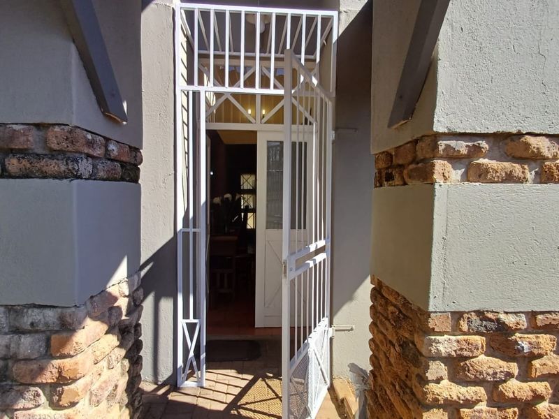 Entrance area featuring a white security gate and timber door framed by rustic brick pillars.