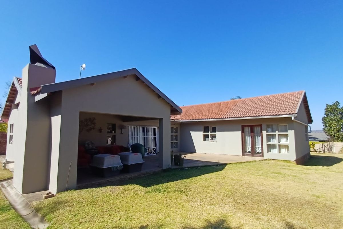 Rear view of the house featuring a covered patio area, tiled roof, and a chimney, set against a spacious lawn.