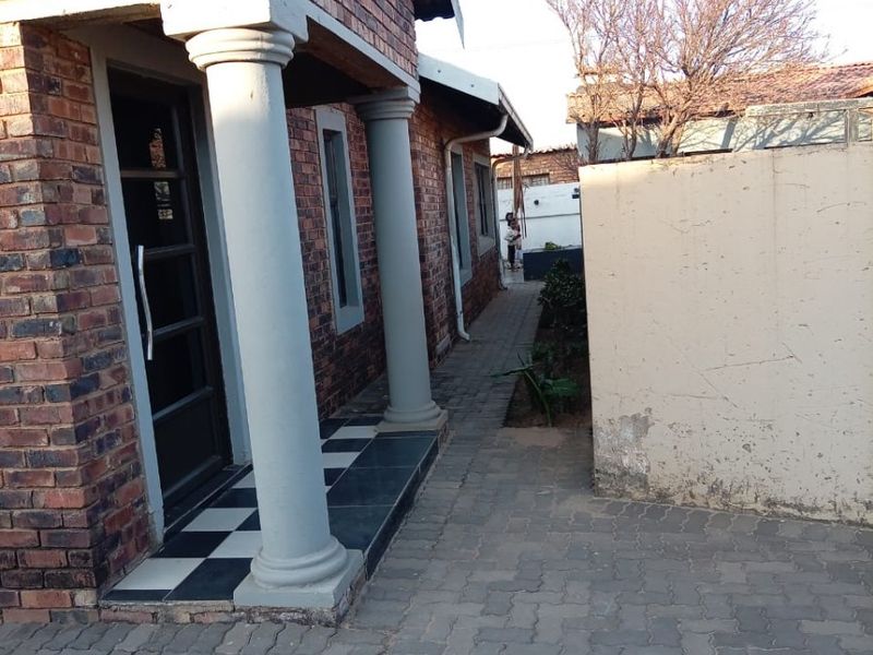 A side view of the property featuring a face brick facade with decorative columns, a paved walkway, and a boundary wall.