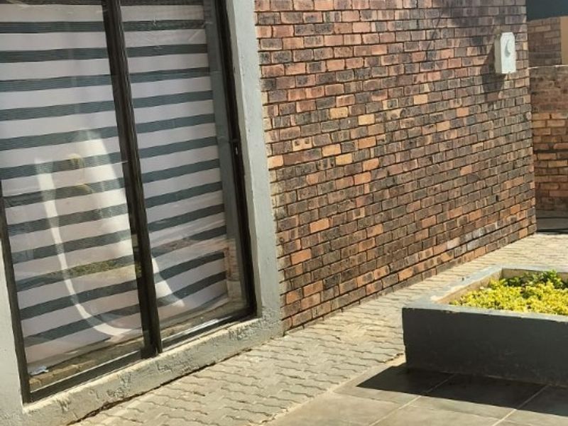 Rear exterior view featuring a face brick wall, sliding glass door, tiled patio area, and a built-in fire pit with a raised planter box.