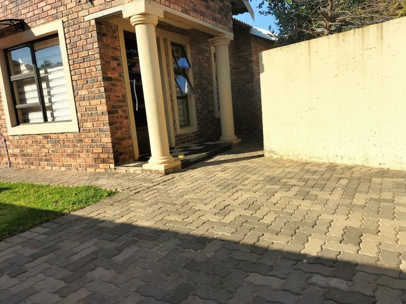 Front exterior view of a face brick house featuring concrete columns, paved driveway, and a boundary wall.