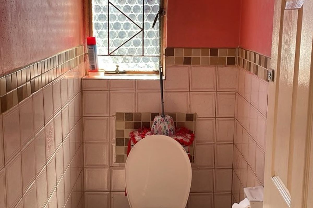 A compact bathroom featuring a toilet, tiled wall accents, and a window with a security gate.