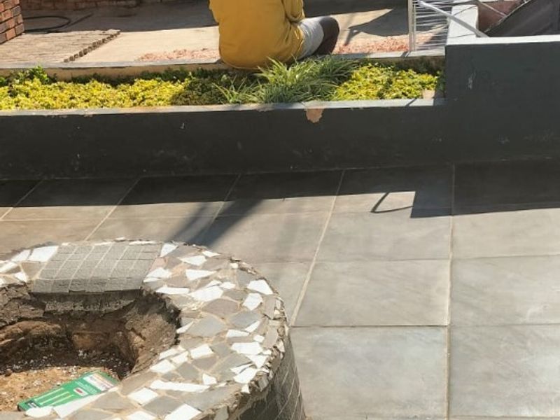 Outdoor patio area featuring tiled flooring, a brick boundary wall, a raised garden bed, and a circular fire pit.