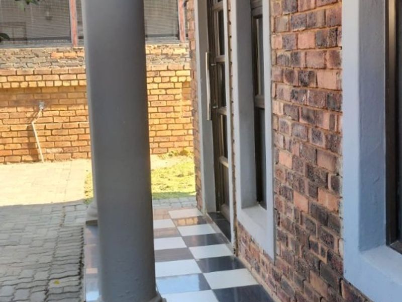 A covered patio area featuring a concrete column, tiled flooring, and exposed brick exterior wall, providing a functional outdoor transition space.